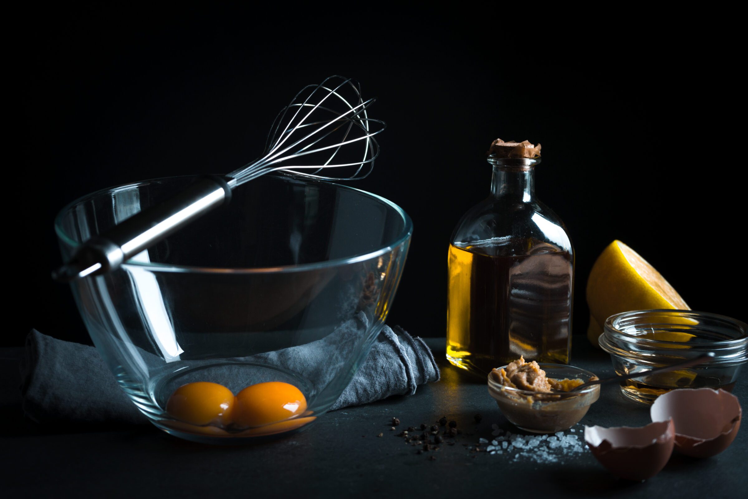 Yolks in a glass bowl, whisk for whipping, olive oil